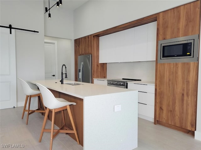 kitchen with a barn door, stainless steel appliances, a sink, white cabinets, and light countertops