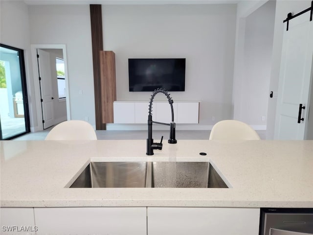 kitchen with light stone counters, white cabinets, a sink, and a barn door