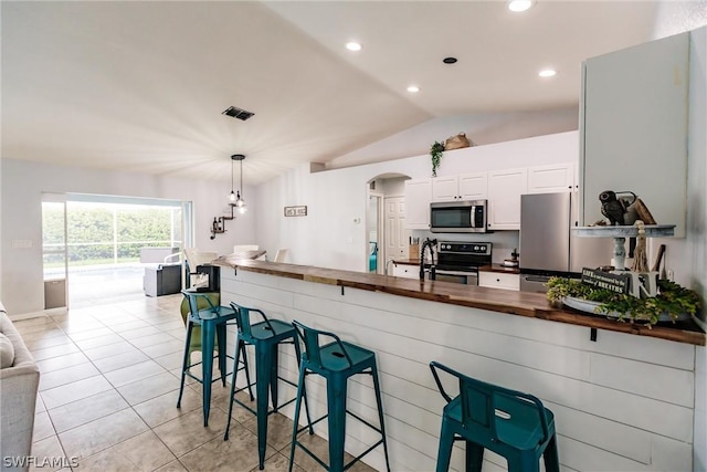 kitchen with wooden counters, white cabinets, hanging light fixtures, a kitchen bar, and stainless steel appliances