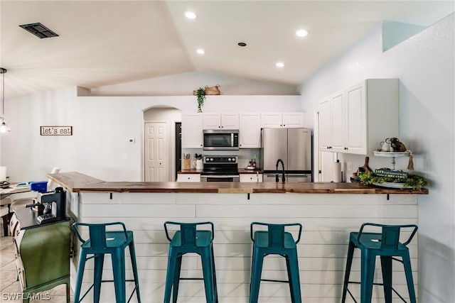 kitchen with a kitchen bar, white cabinets, stainless steel appliances, and vaulted ceiling