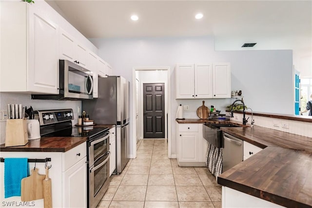 kitchen with wood counters, white cabinets, light tile patterned flooring, and appliances with stainless steel finishes