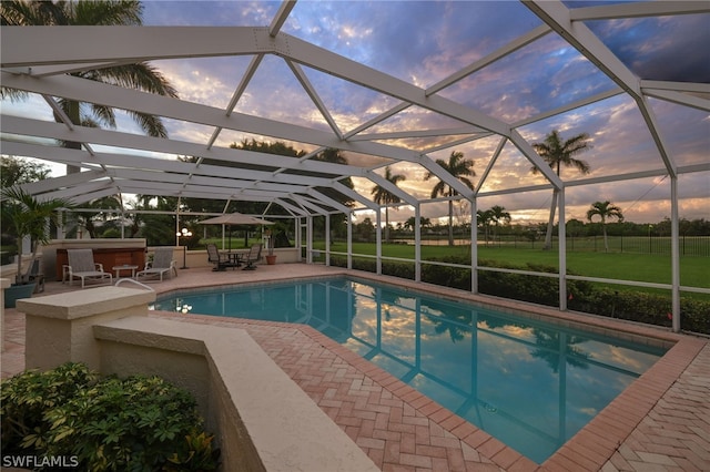 pool at dusk with a lawn, glass enclosure, a patio, and a hot tub