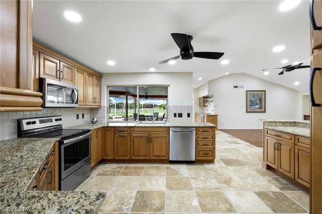 kitchen featuring backsplash, light stone counters, lofted ceiling, and appliances with stainless steel finishes