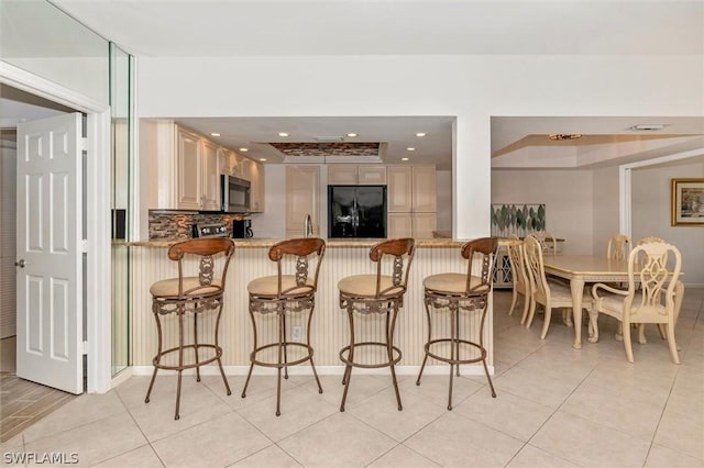 kitchen featuring kitchen peninsula, black refrigerator with ice dispenser, a breakfast bar area, and light tile patterned flooring