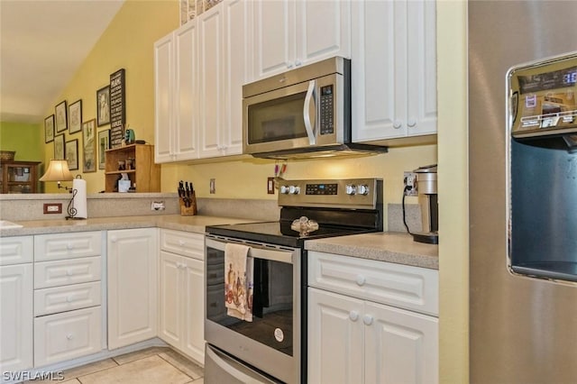 kitchen featuring appliances with stainless steel finishes, white cabinetry, lofted ceiling, and light tile patterned flooring