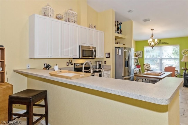 kitchen with kitchen peninsula, a breakfast bar, stainless steel appliances, white cabinetry, and hanging light fixtures