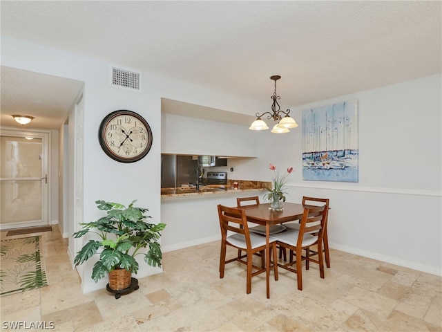 dining area with sink, a textured ceiling, and an inviting chandelier