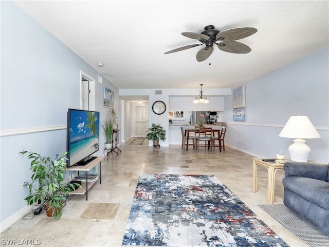 living room featuring ceiling fan with notable chandelier and a textured ceiling