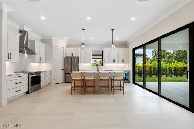 kitchen with appliances with stainless steel finishes, wall chimney range hood, decorative light fixtures, white cabinets, and a kitchen island