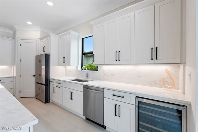 kitchen with sink, beverage cooler, appliances with stainless steel finishes, white cabinets, and ornamental molding