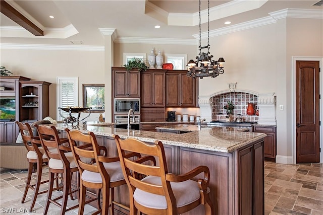 kitchen with a notable chandelier, a raised ceiling, light stone counters, and a large island with sink