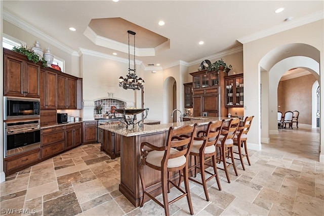 kitchen with oven, a raised ceiling, a spacious island, light stone countertops, and black microwave