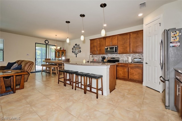 kitchen with stainless steel appliances, an island with sink, pendant lighting, stone countertops, and a breakfast bar area