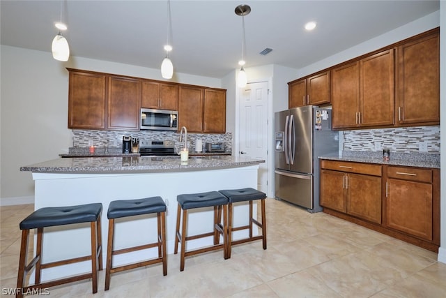 kitchen featuring sink, stainless steel appliances, decorative light fixtures, a kitchen bar, and a center island with sink