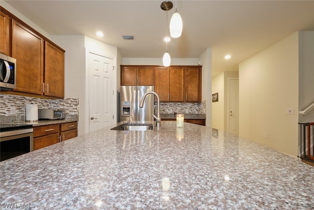 kitchen featuring sink, hanging light fixtures, stainless steel appliances, light stone counters, and backsplash