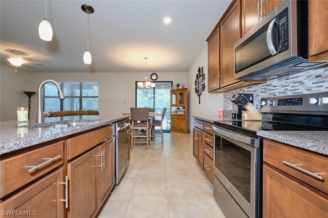 kitchen featuring light stone countertops, backsplash, stainless steel appliances, sink, and hanging light fixtures