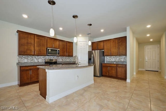 kitchen featuring brown cabinets, stainless steel appliances, tasteful backsplash, hanging light fixtures, and a kitchen island with sink