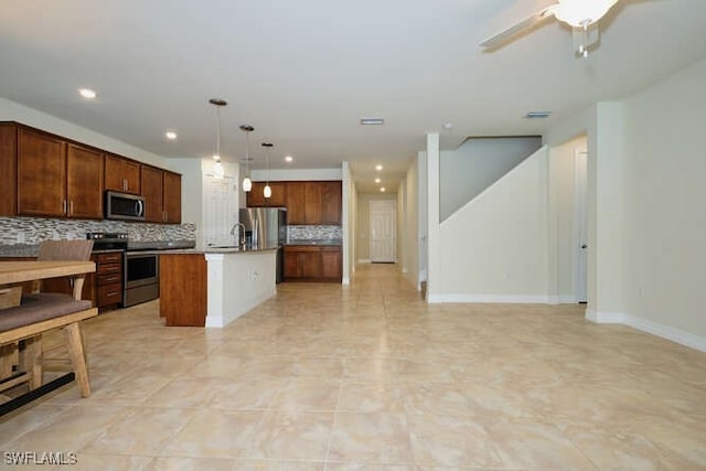 kitchen with tasteful backsplash, appliances with stainless steel finishes, open floor plan, decorative light fixtures, and a kitchen island with sink