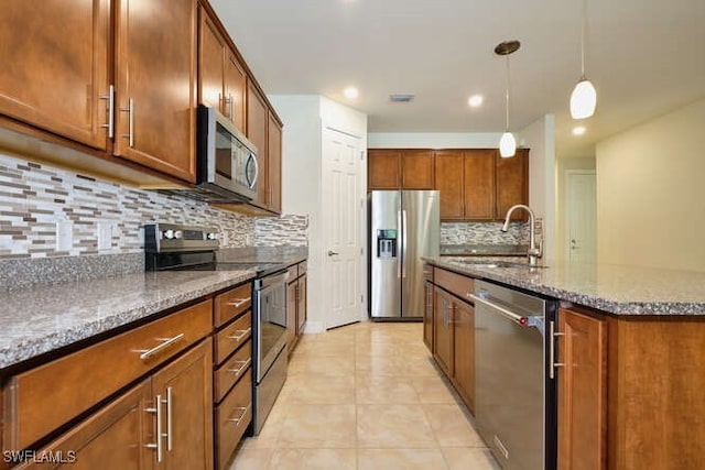 kitchen featuring stainless steel appliances, decorative light fixtures, a sink, and dark stone countertops