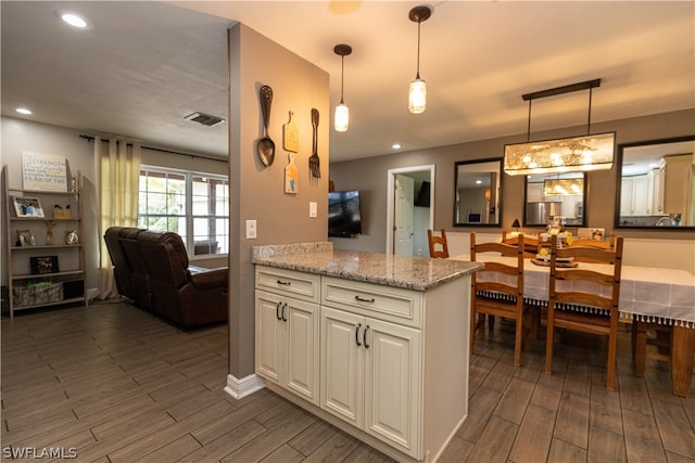 kitchen with dark hardwood / wood-style flooring, light stone countertops, cream cabinetry, and hanging light fixtures