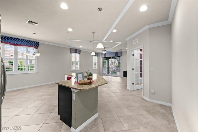 kitchen with ceiling fan, hanging light fixtures, light stone counters, crown molding, and a center island with sink