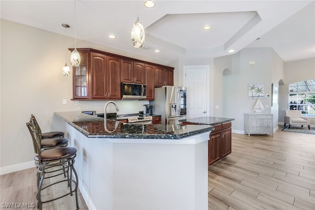 kitchen featuring pendant lighting, a breakfast bar area, light hardwood / wood-style floors, kitchen peninsula, and stainless steel appliances