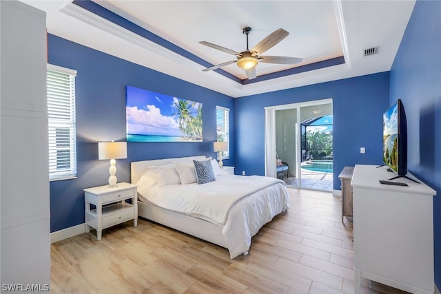 bedroom featuring access to exterior, light hardwood / wood-style floors, a raised ceiling, and ceiling fan