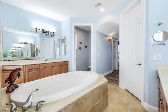 bathroom with vanity, a relaxing tiled tub, and toilet