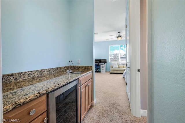 kitchen with light carpet, dark stone counters, ceiling fan, sink, and wine cooler