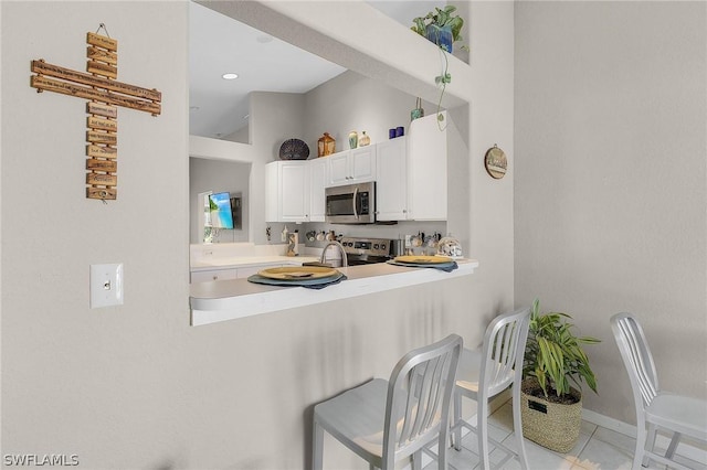 kitchen with stainless steel appliances, light tile patterned floors, kitchen peninsula, a breakfast bar area, and white cabinets