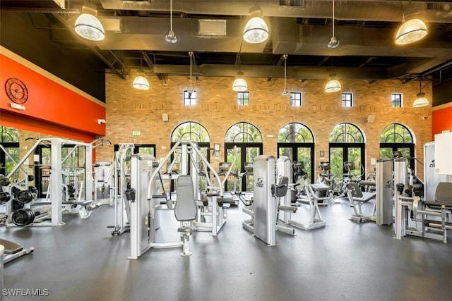 workout area with a high ceiling, a healthy amount of sunlight, and brick wall