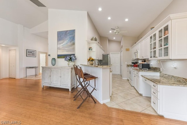 kitchen featuring white appliances, kitchen peninsula, light stone countertops, white cabinetry, and a breakfast bar area