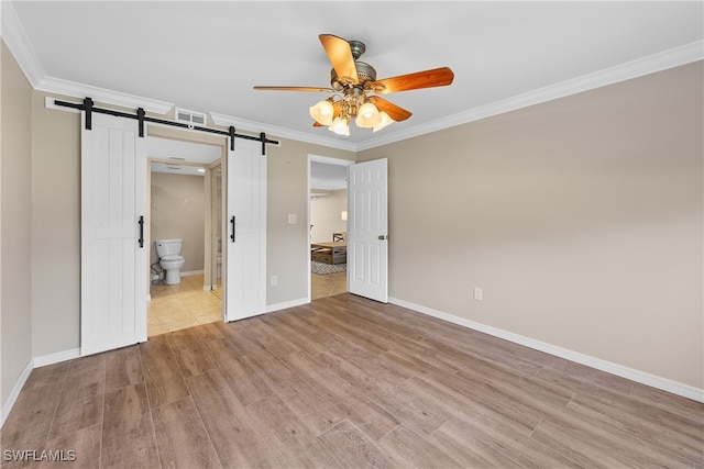 unfurnished bedroom with ceiling fan, light wood-type flooring, ensuite bath, and a barn door