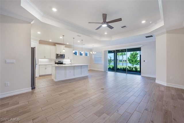 kitchen with a kitchen island with sink, white cabinets, appliances with stainless steel finishes, a tray ceiling, and decorative light fixtures