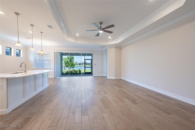 unfurnished living room featuring ornamental molding, sink, ceiling fan with notable chandelier, and a tray ceiling