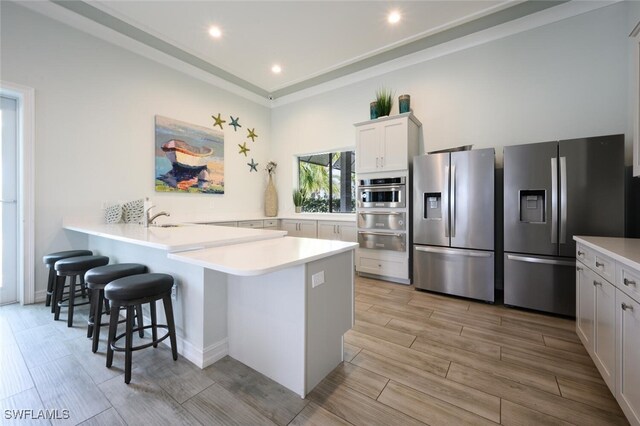 kitchen with kitchen peninsula, appliances with stainless steel finishes, sink, white cabinets, and a breakfast bar area