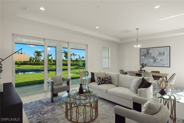 living room featuring a raised ceiling, a water view, and hardwood / wood-style floors