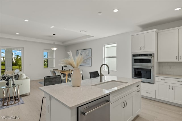 kitchen featuring decorative light fixtures, white cabinetry, sink, stainless steel appliances, and a center island with sink