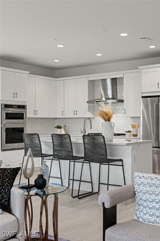 kitchen with appliances with stainless steel finishes, a breakfast bar, wall chimney range hood, and white cabinets