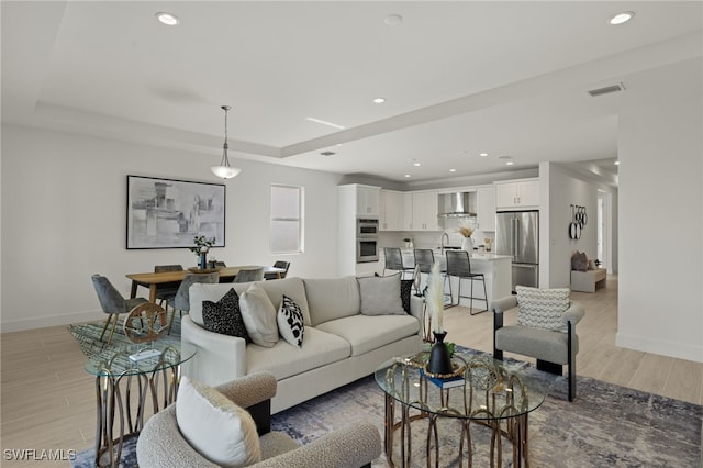 living room with sink, a tray ceiling, and light wood-type flooring