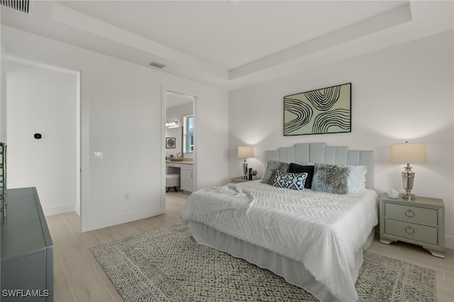 bedroom featuring ensuite bath and a raised ceiling