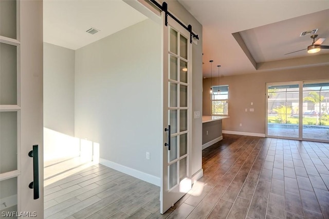 empty room featuring a raised ceiling, a barn door, and ceiling fan