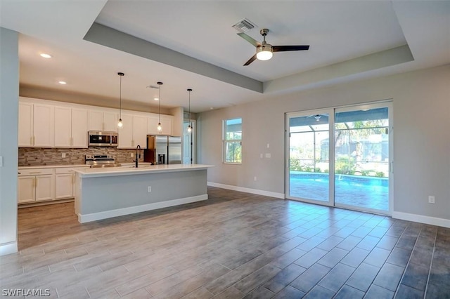 kitchen with a raised ceiling, white cabinetry, appliances with stainless steel finishes, and an island with sink