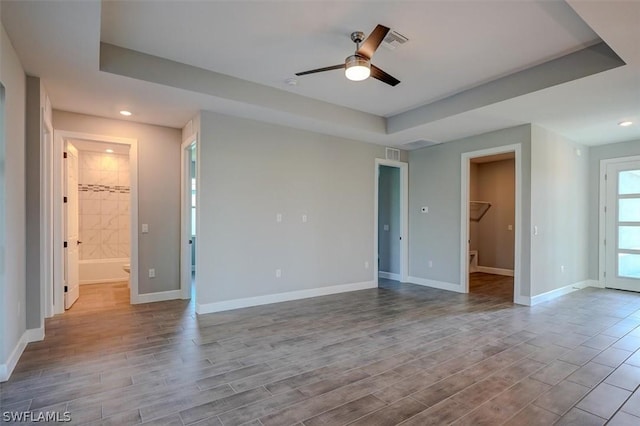 unfurnished room with ceiling fan, light hardwood / wood-style floors, and a tray ceiling