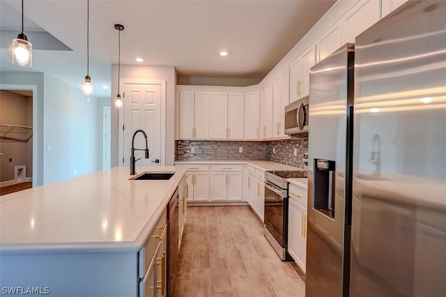 kitchen featuring sink, hanging light fixtures, an island with sink, stainless steel appliances, and white cabinets