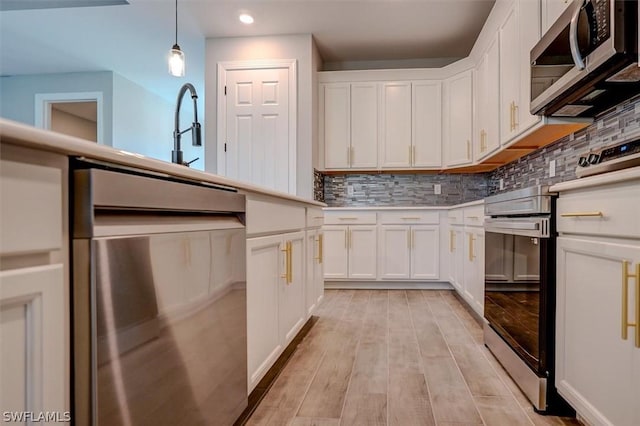 kitchen featuring stainless steel appliances, tasteful backsplash, white cabinets, and decorative light fixtures