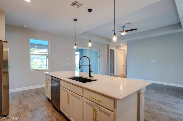 kitchen with pendant lighting, a raised ceiling, an island with sink, sink, and stainless steel appliances