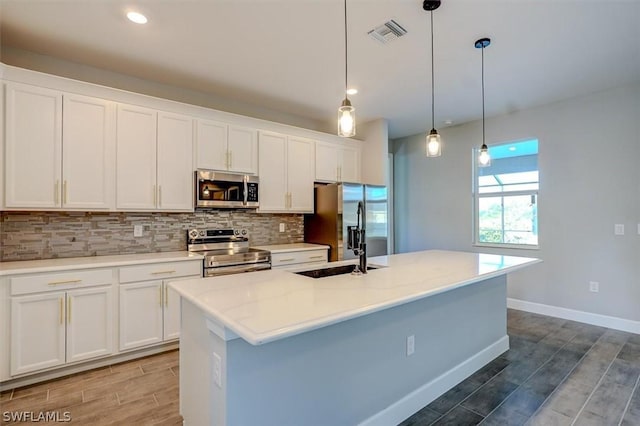 kitchen featuring white cabinetry, appliances with stainless steel finishes, pendant lighting, and a center island with sink