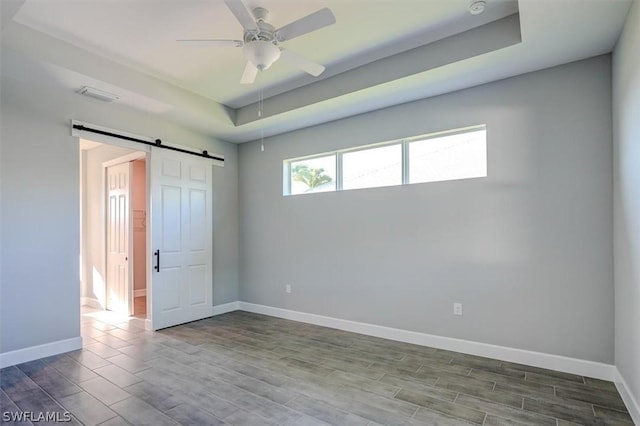 empty room with a tray ceiling, a barn door, and ceiling fan