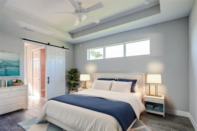 bedroom featuring ceiling fan, a barn door, and a raised ceiling